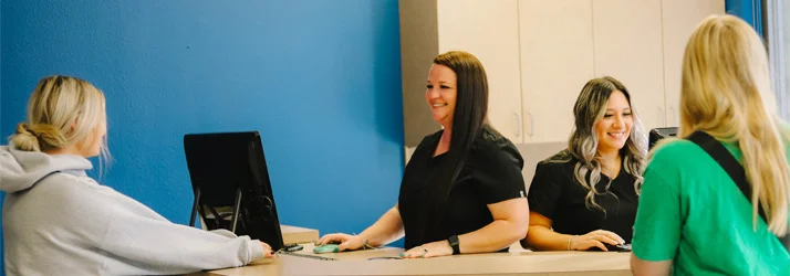 Chiropractic Allen TX Frequently Asked Questions Front desk staff checking in patients with a blue wall behind them.