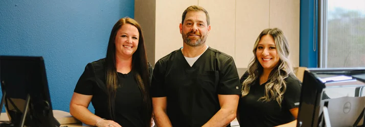 Chiropractor Michael Wojnicki smiling with two front desk staff.